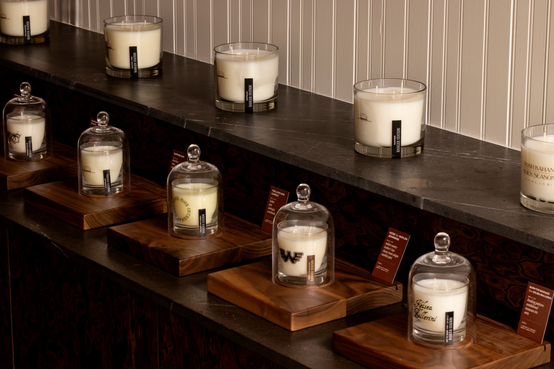 Ranger Station candles under glass cloches on stone display steps, including Hoss, Stick Season, and Burn the Baggage.
