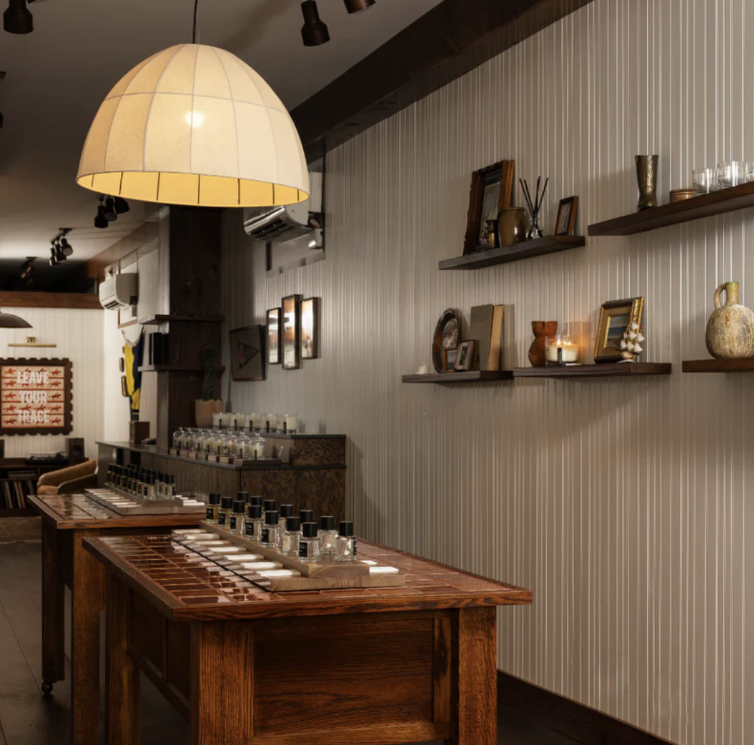 The Ranger Station Charleston house — perfume tables under a domed pendant lamp, shelves of candles and framed art along a beadboard wall.